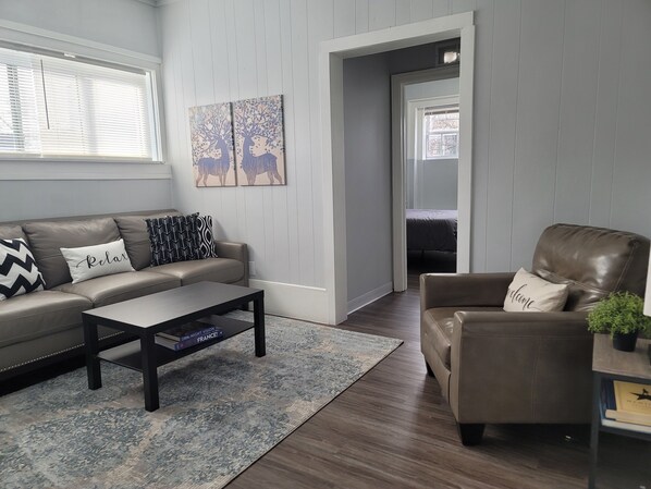 A living room with a sofa, armchair, coffee table, and artwork on the wall.