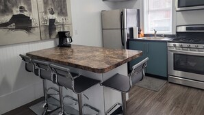 Una cocina compacta con encimera de mármol, taburetes de bar, un refrigerador, una estufa y una cafetera.