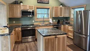 Une cuisine dotée de meubles en bois, d’appareils électroménagers en acier inoxydable, d’un plan de travail en granit et d’une fenêtre donnant sur un paysage verdoyant.