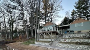 Une maison à deux étages, avec des fondations en pierre, un porche couvert et un étang en premier plan.