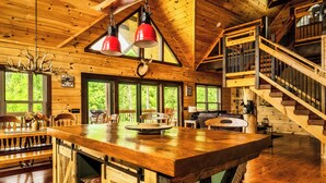 A wooden cabin interior with a large dining table, wooden staircase, and large windows offering a view of the forest. - Mountain View l 3mi to Gatlinburg l Hot Tub l Game Room l Pack N Play (Gatlinburg)