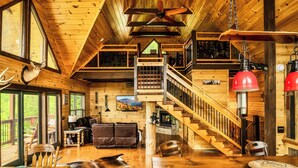 A log cabin interior with a wooden staircase, leather furniture, and a dining area with a fur rug. - Mountain View l 3mi to Gatlinburg l Hot Tub l Game Room l Pack N Play (Gatlinburg)