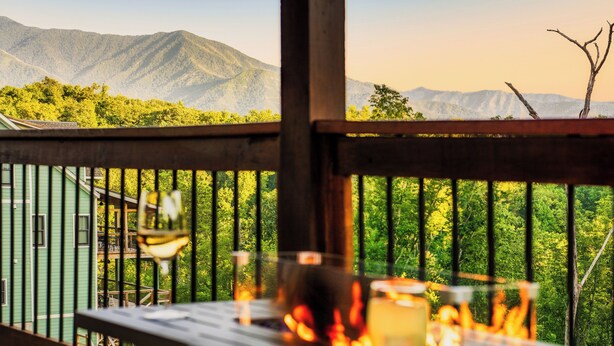 A deck with a view of mountains and trees, a glass of drink, and a candle. - Mountain View l 3mi to Gatlinburg l Hot Tub l Game Room l Pack N Play (Gatlinburg)
