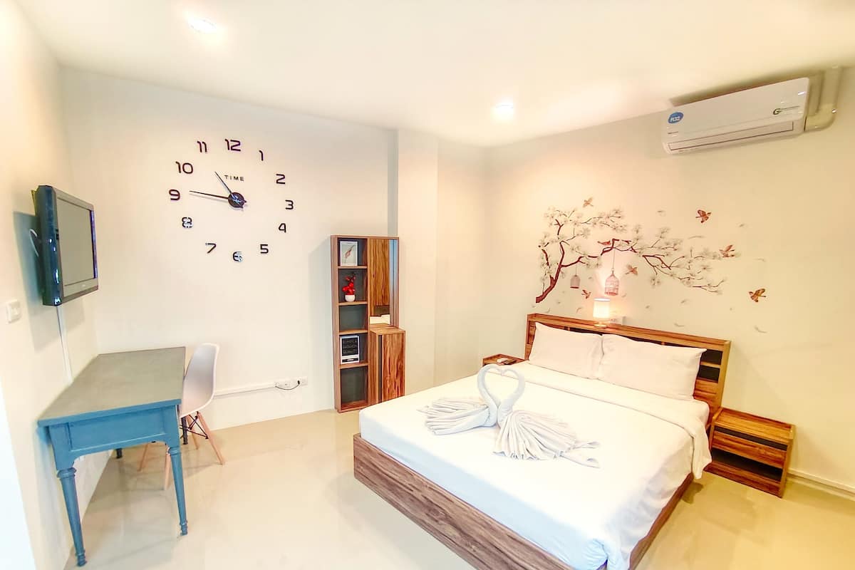 Une chambre à coucher comprenant un lit, un bureau, une chaise, une horloge murale et un climatiseur fixé au mur.