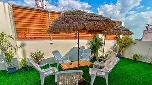 A patio with artificial grass, white plastic chairs, a wooden table, and a thatched umbrella. - Sailor Hotel Pattaya - Nice Rooms & Steps to Walking Street (Pattaya)