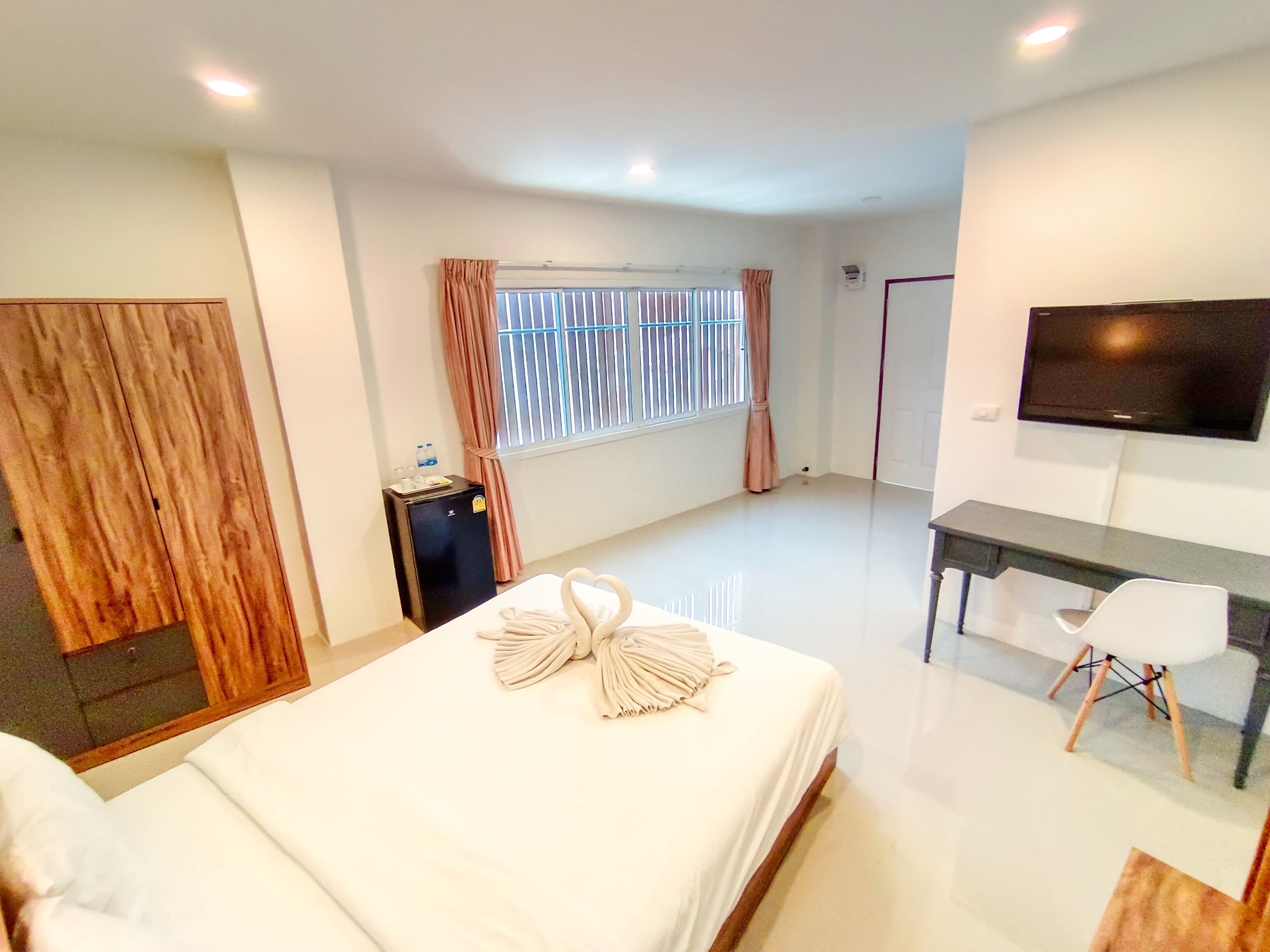 Habitación de hotel con cama, escritorio, televisor y ventana con cortinas.
