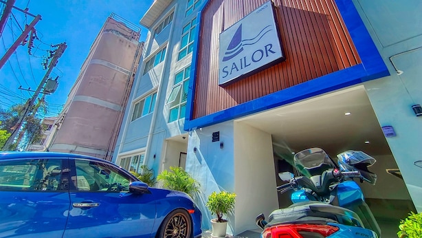 A building with a sign reading "SAILOR" and a blue car parked in front. - Sailor Hotel Pattaya - Nice Rooms & Steps to Walking Street (Pattaya)