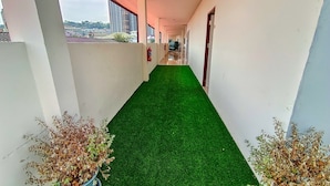 A corridor with artificial green flooring, white walls, and potted plants on either side. - Sailor Hotel Pattaya - Nice Rooms & Steps to Walking Street (Pattaya)