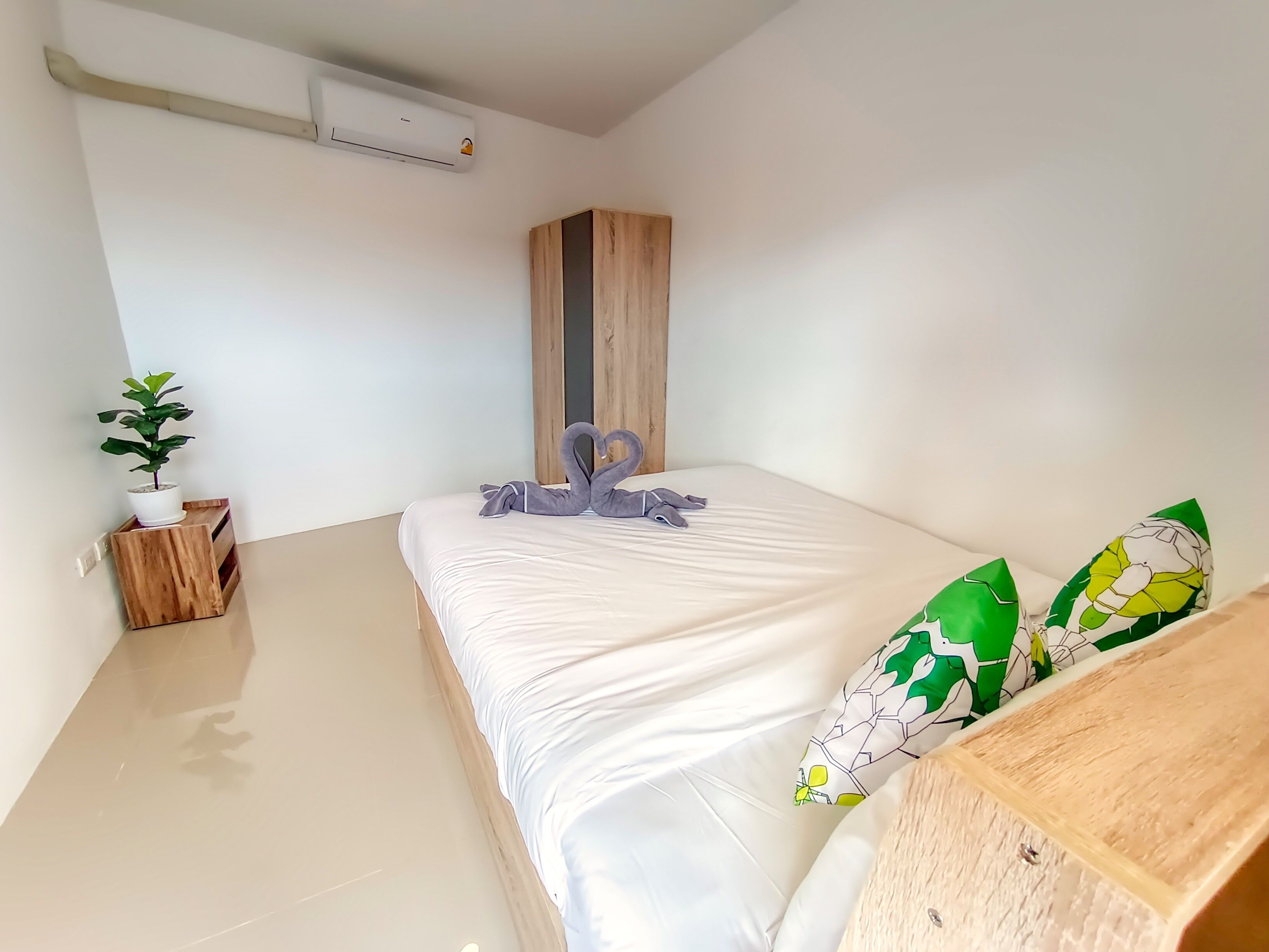 A modern bedroom with a bed, a wooden nightstand, a potted plant, and a wall-mounted air conditioner.