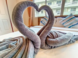 A bed with a heart-shaped towel arrangement and a view of a building with balconies. - Sailor Hotel Pattaya - Nice Rooms & Steps to Walking Street (Pattaya)