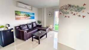 A modern living room with a leather sofa, a coffee machine, and a painting of a beach scene. - Sailor Hotel Pattaya - Nice Rooms & Steps to Walking Street (Pattaya)