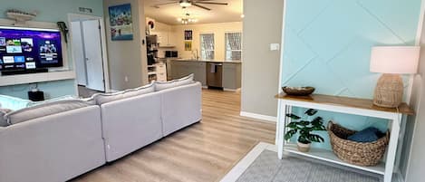 A modern living room with a sectional sofa, a flat-screen TV, and a kitchen in the background.