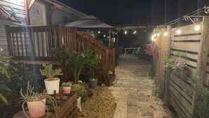 Une terrasse en bois agrémentée de plantes en pot, un chemin de pierres et des guirlandes lumineuses.