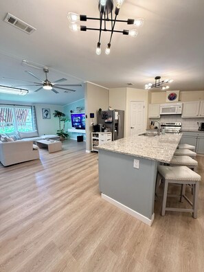 A modern kitchen with a central island, white cabinetry, and a dining area with a sofa and coffee table.