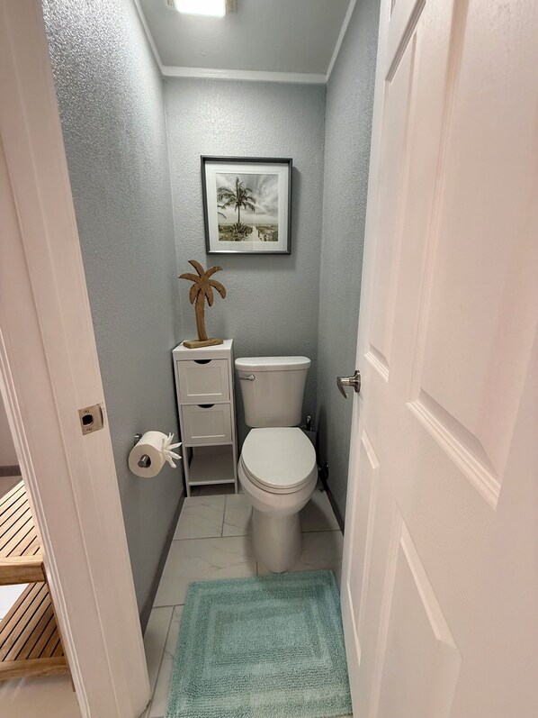 A small bathroom with a toilet, a framed picture on the wall, and a wooden palm tree decoration.