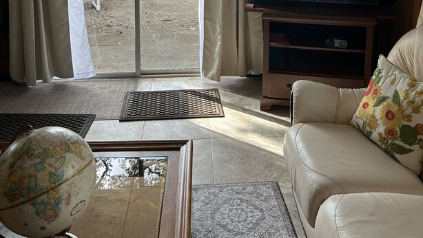 A living room with a television, a sofa, a chair, and a view of a body of water through a sliding door. - Furnished, lakefront 2/1 house in Ocala Nat'l Forest (Silver Springs)