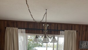 A dining area with a table set for four, surrounded by wooden chairs. A chandelier hangs above, and the room has wooden paneling on the walls. - Furnished, lakefront 2/1 house in Ocala Nat'l Forest (Silver Springs)