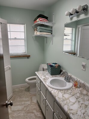 A bathroom with a toilet, sink, and a towel rack with folded towels. - Furnished, lakefront 2/1 house in Ocala Nat'l Forest (Silver Springs)