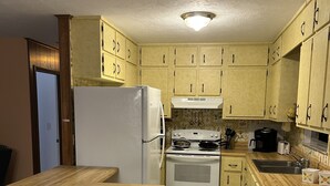 A compact kitchen with wooden cabinets, a white refrigerator, a stove, and a sink. - Furnished, lakefront 2/1 house in Ocala Nat'l Forest (Silver Springs)