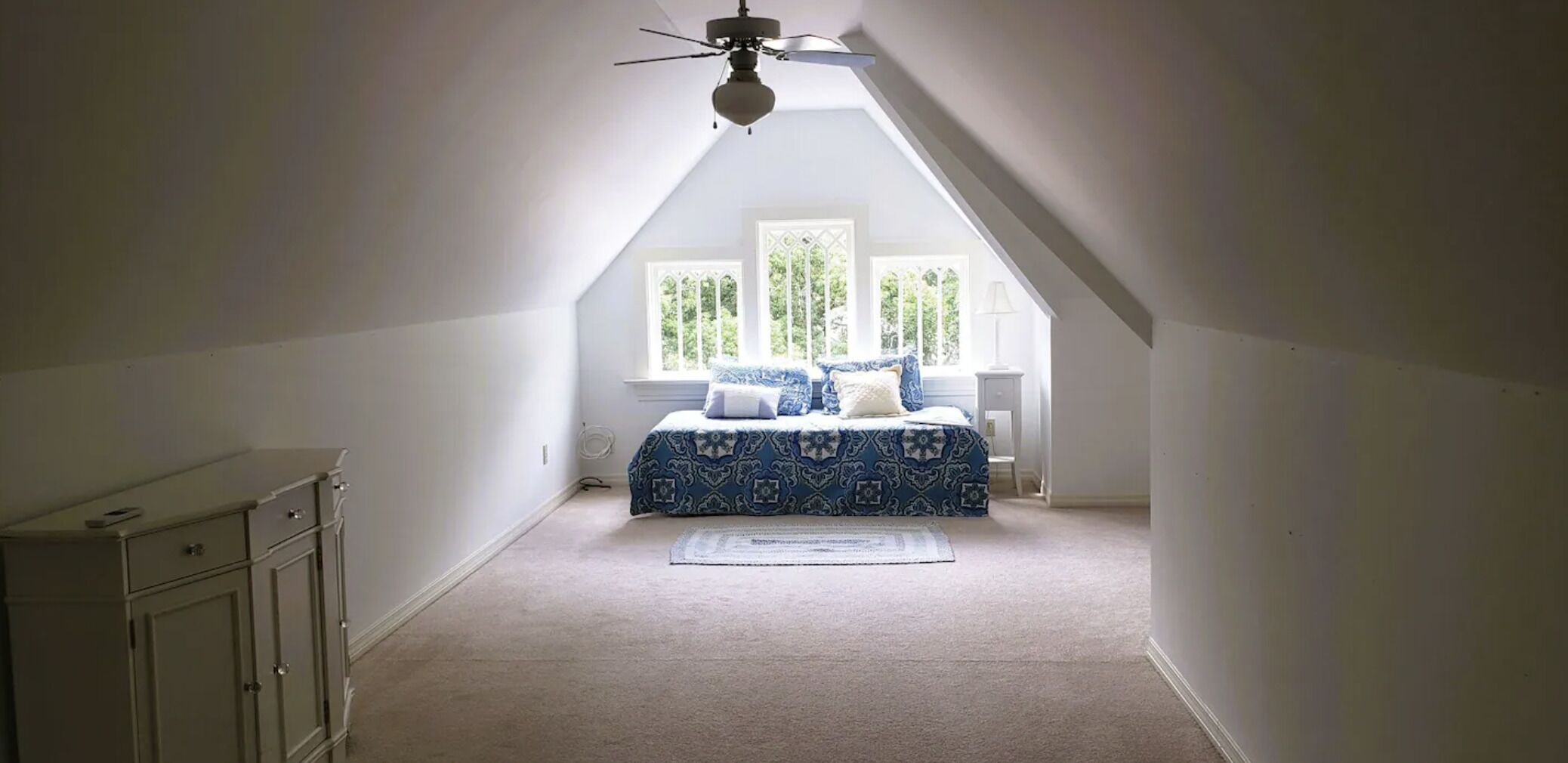 Une chambre avec un plafond en pente, un lit recouvert d’une couvre-lit à motifs, une table de chevet et une fenêtre donnant sur des arbres.