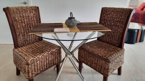 A dining table with two wicker chairs, a glass top, and a decorative vase. - Renovated 2-Bed Cottage - Sleeps 4 - Free Parking (Witta)