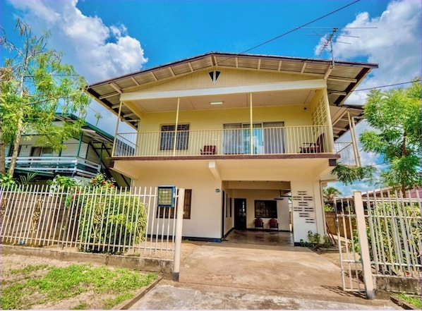 A two-story house with a balcony, a gated entrance, and a clear sky.
