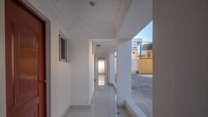 A corridor with a red door, white walls, and a tiled floor leading to a door at the end.