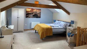 A bedroom with a sloped ceiling, a bed with a yellow blanket, a desk with a computer, a chair, a radiator, and a wall-mounted artwork. - 1 bed-cottage-Parking-Patio-close to coasts (Launceston)