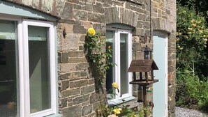 A stone building with a window, a bird feeder, and yellow flowers. - 1 bed-cottage-Parking-Patio-close to coasts (Launceston)