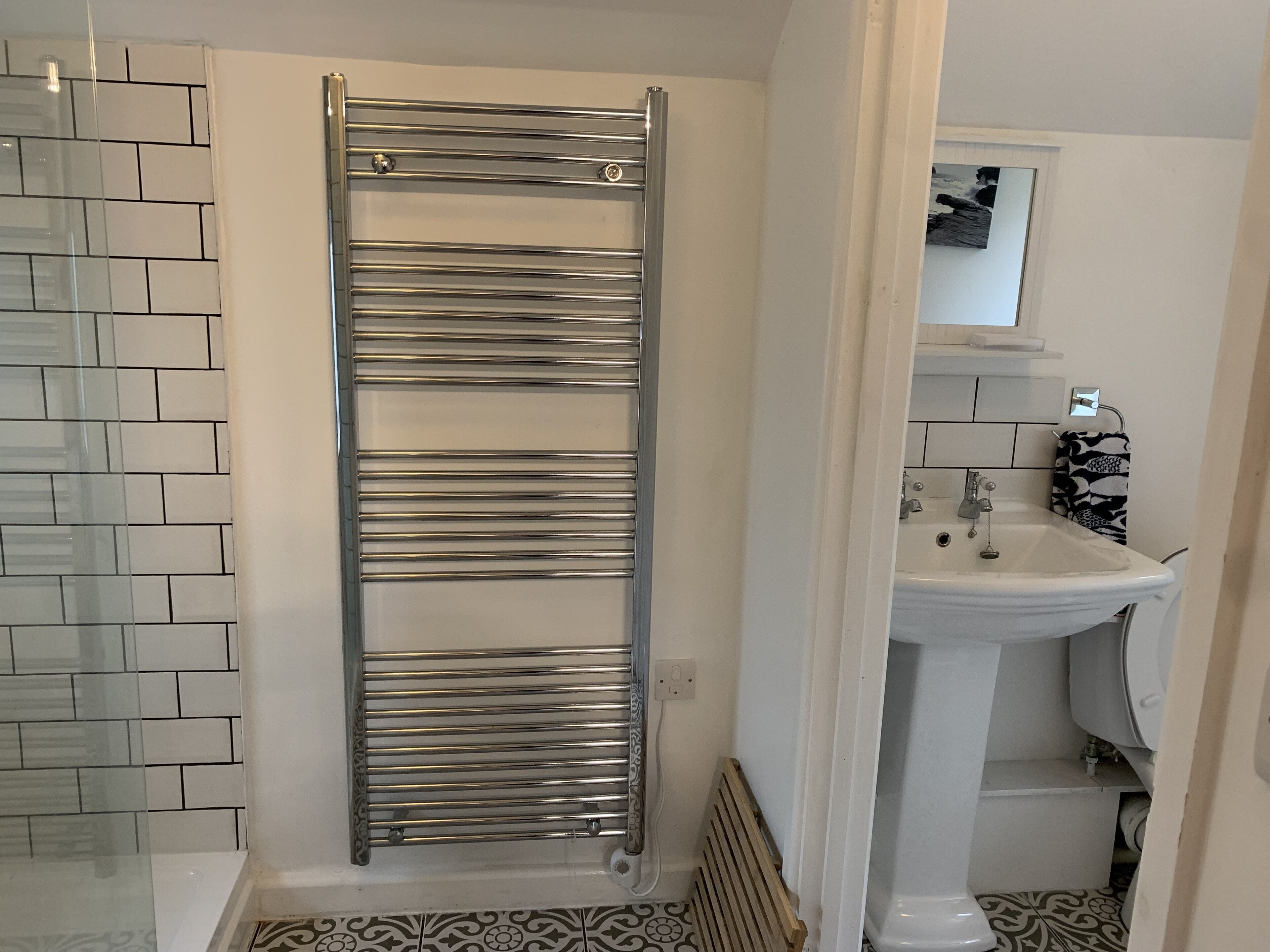 A bathroom with a glass shower enclosure, a chrome towel rack, a white sink, and patterned floor tiles.