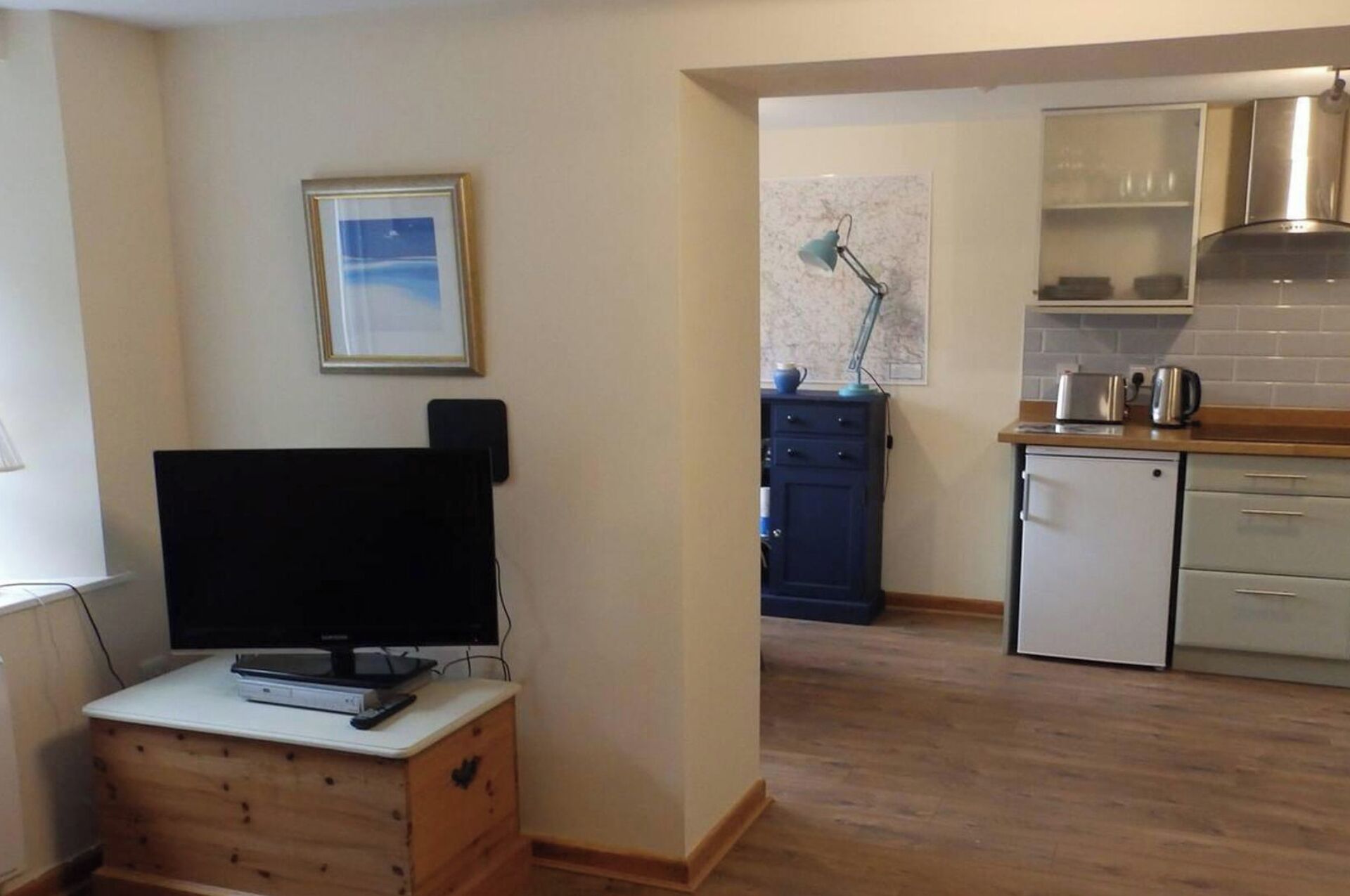 Un espacio habitable pequeño con kitchenette, televisor y un cuadro en la pared.
