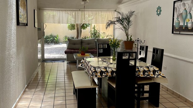 Un vaste espace dédié à la salle à manger, doté d’un sol carrelé, d’un ventilateur de plafond et d’une table à manger recouverte d’une nappe à motifs.