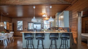 A modern kitchen with wooden paneling, a central island with bar stools, and pendant lighting. - Lake Oconee Lake Front Cabin+Private Dock+Fire Pit+Fireplace+AMAZING VIEWS! (Eatonton)