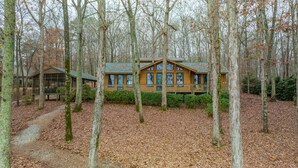 A cabin with a large window, surrounded by trees and a leaf-covered ground. - Lake Oconee Lake Front Cabin+Private Dock+Fire Pit+Fireplace+AMAZING VIEWS! (Eatonton)
