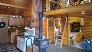 Interno accogliente di una baita con angolo cottura, sala da pranzo e soppalco caratterizzato da un soffitto in legno e una grande ruota.