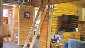 Interno di una baita in legno con scala in legno, angolo cottura e soggiorno con divano.