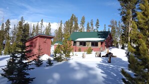 Una baita rossa con tetto verde, circondata da neve e alberi.