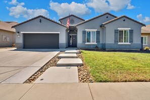 Une maison à deux étages avec un garage, une pelouse devant et un chemin menant à l’entrée.