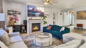 A modern living room with a fireplace, a ceiling fan, and a large TV. - Family Pool Home – Saltwater Pool & Fire Pit – 2 King Suites – Sleeps 12 (Elk Grove)