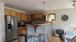 Een moderne keuken met houten kastjes, een roestvrijstalen koelkast, een inbouw eiland met krukken en een eethoek met een tafel en stoelen.