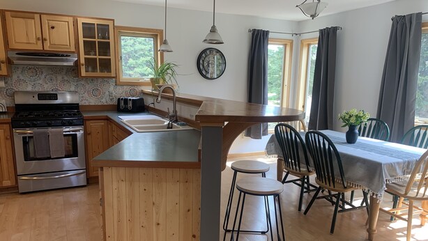 Een moderne keuken met houten kastjes, een inbouwoven, een spoelbak en een eethoek met tafel en stoelen.