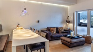 A modern living room with a dining table, sofa, and ottoman, large windows with a view, and a pendant light. - Apartment "Haus Excelsior Top 38" with Mountain View, Balcony & Wi-Fi (Seefeld in Tirol)