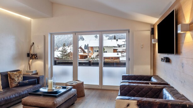 A modern living room with a sofa, ottoman, and a flat-screen TV mounted on the wall. - Apartment "Haus Excelsior Top 38" with Mountain View, Balcony & Wi-Fi (Seefeld in Tirol)