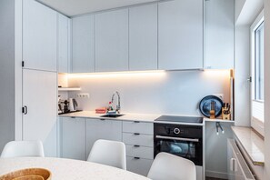 Una cocina moderna con horno empotrado, lavamanos y comedor con sillas blancas.