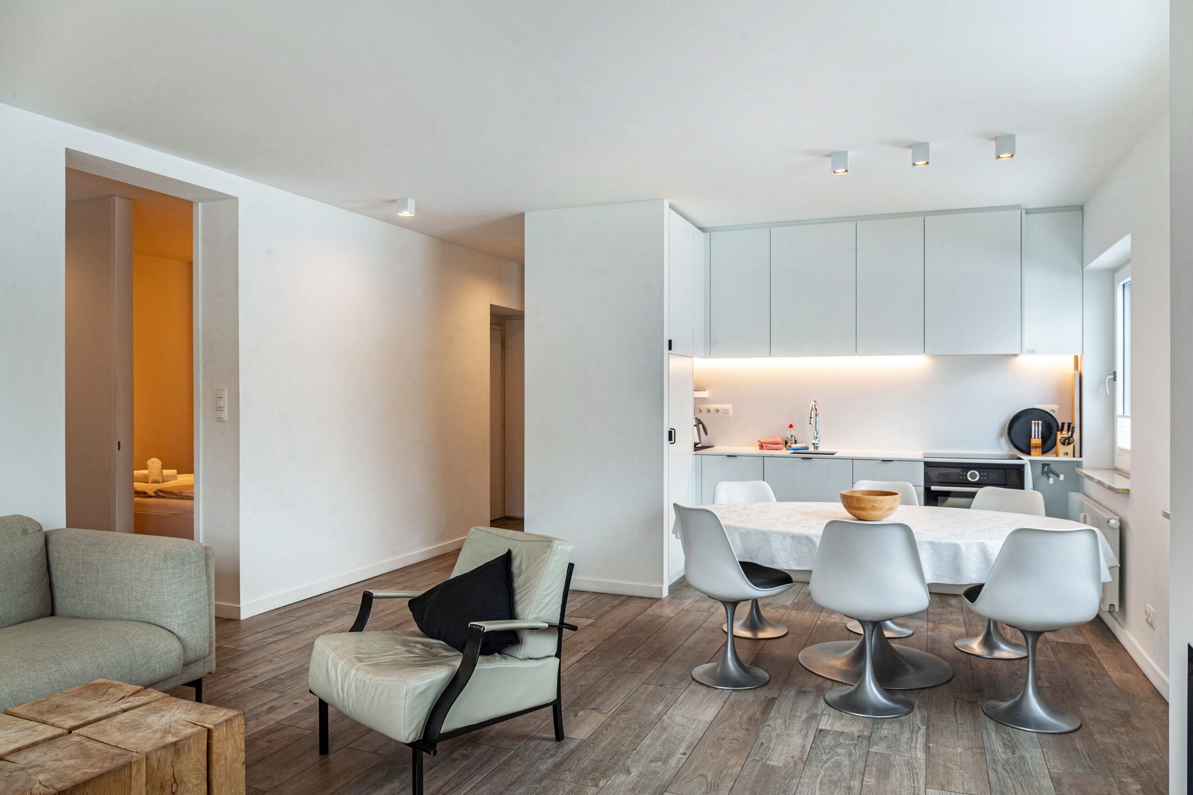 A modern living room with a sofa, a dining table with chairs, and a kitchen area with cabinets and a countertop.