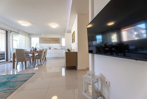 Een moderne keuken met witte kasten, een eethoek met een tafel en stoelen, en een groot raam.