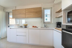 Een moderne keuken met witte kasten, een houten bovenkast, een raam en een inbouwoven.