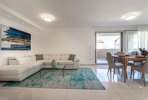 Een moderne woonkamer met een hoekbank, een salontafel en een eethoek met een tafel en stoelen.