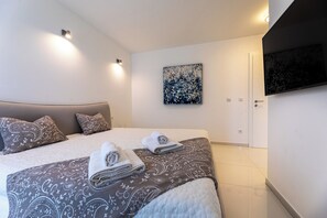 Een slaapkamer met een bed, kussens, handdoeken, een schilderij en een televisie.