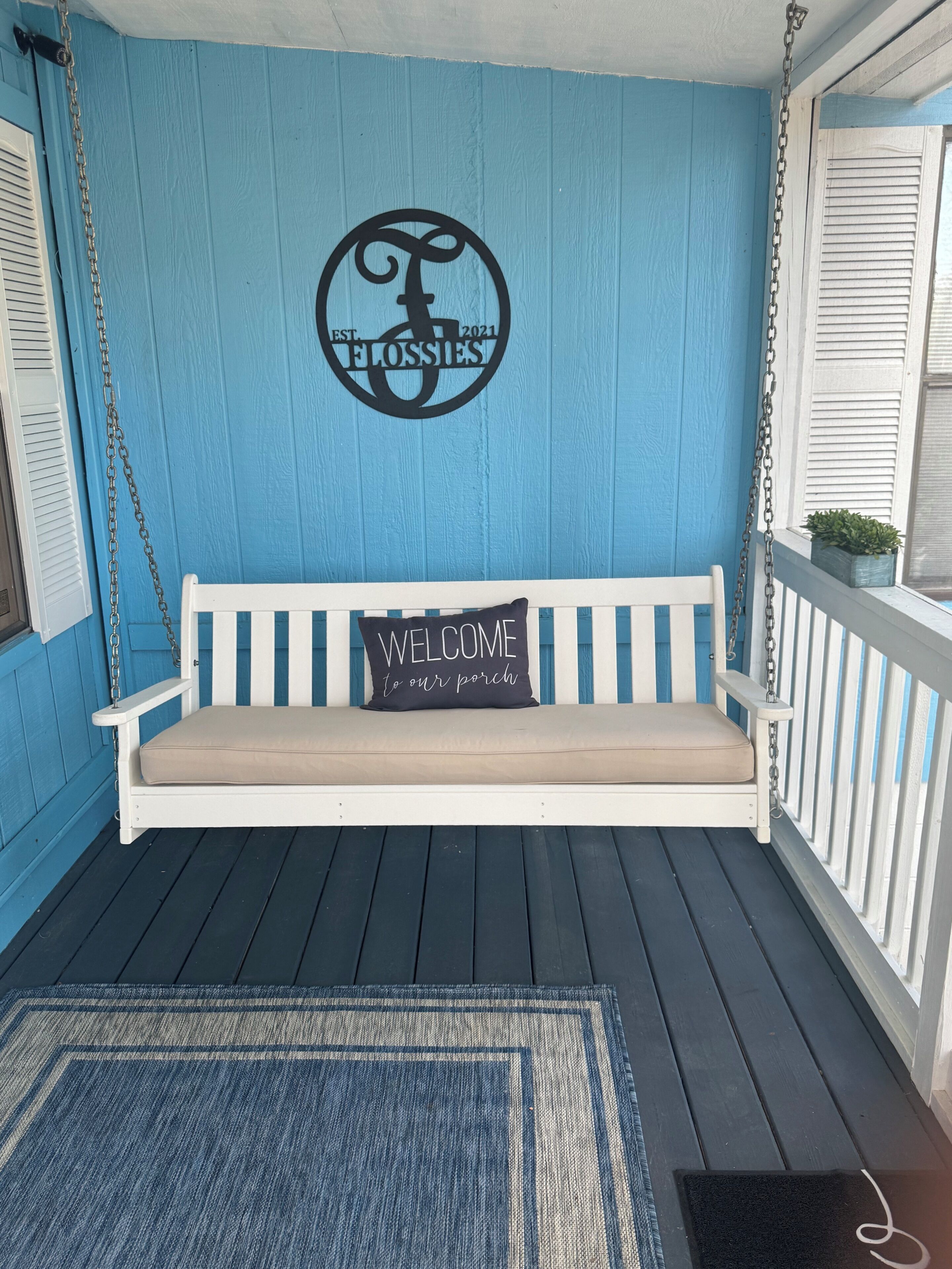 A porch with a white swing bench, a welcome sign, and a logo on the wall.